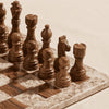 A decorative chess set with a distressed stone-look board and pieces, photographed on a warm beige fabric background with soft shadows.