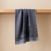 Curiosités Minérales jacquard tea towel draped over an oak edge, showing how the cloth hangs