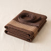 Barista apron folded with its waist ties coiled on top, the woven stripe band across the bib