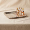 A polished silver rectangular serving tray with raised edges and small feet, displayed on a draped beige fabric background.