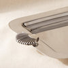 A polished silver rectangular serving tray with decorative shell-shaped handles, resting on a draped cream fabric background.