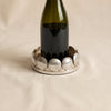 A silver-toned circular tray or dish with a decorative border of scalloped shell-like segments, photographed on a soft beige fabric background.